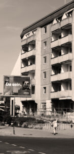 Fotografie von Alexander Ali Rönisch. Aufnahme eines Hochhauses. Davor ein Werbeplakat der Lufthansa mit der Aufschrift "Da sein."